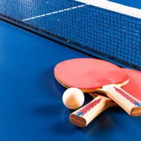 zwei rote Tischtennisschläger und ein Ball liegen auf einer blauen Platte vorm Netz